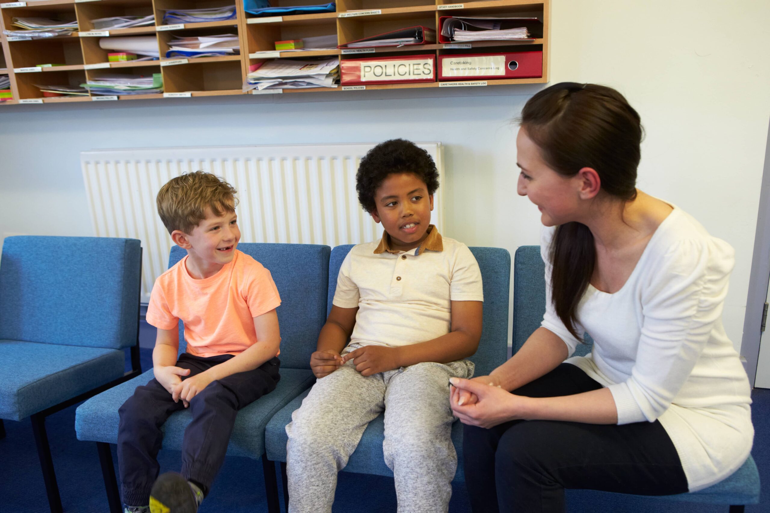 Two students sit in chairs, talking with school counselor in a school office