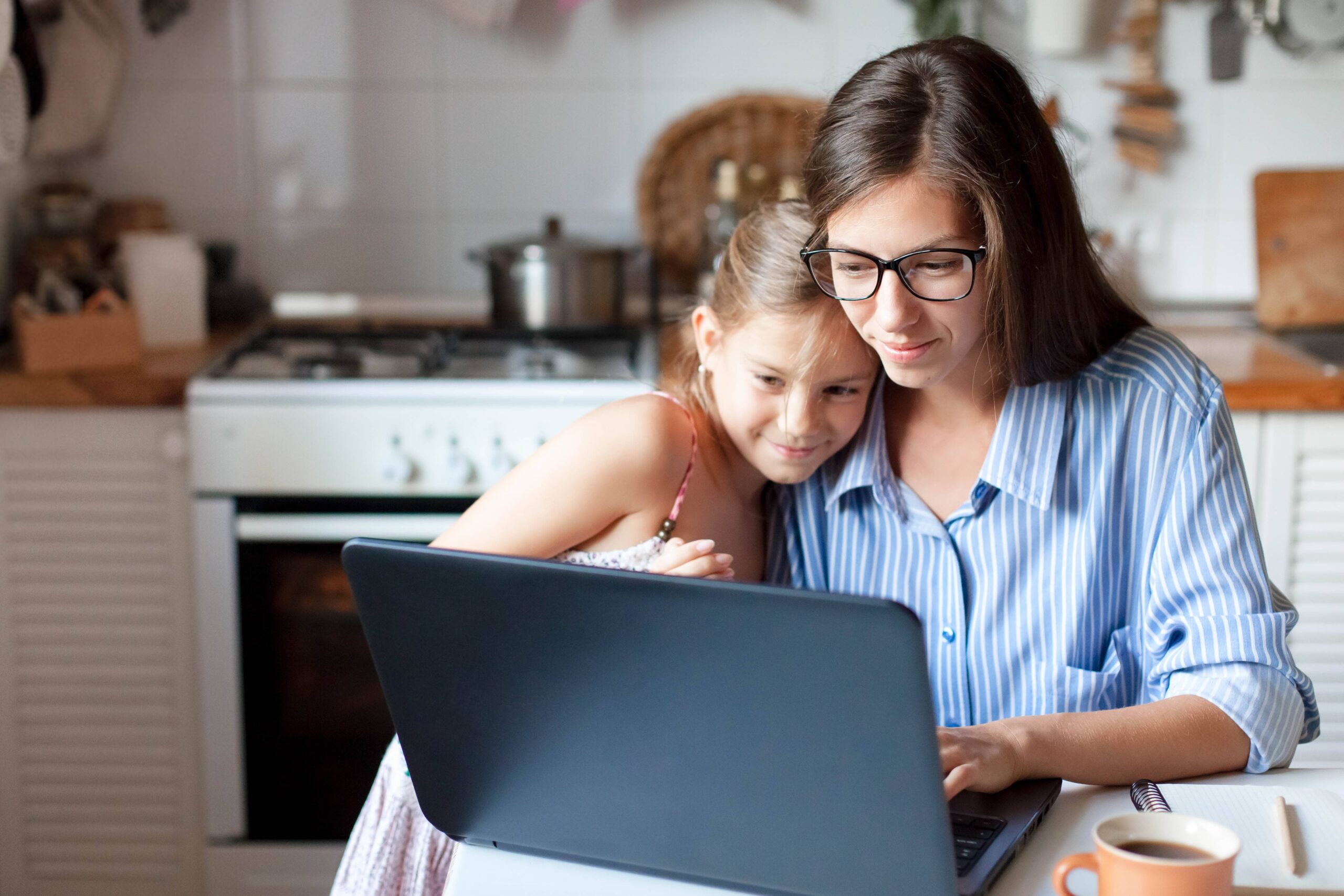 A Mother and Daughter look happy as they use a laptop in their kitchen at home